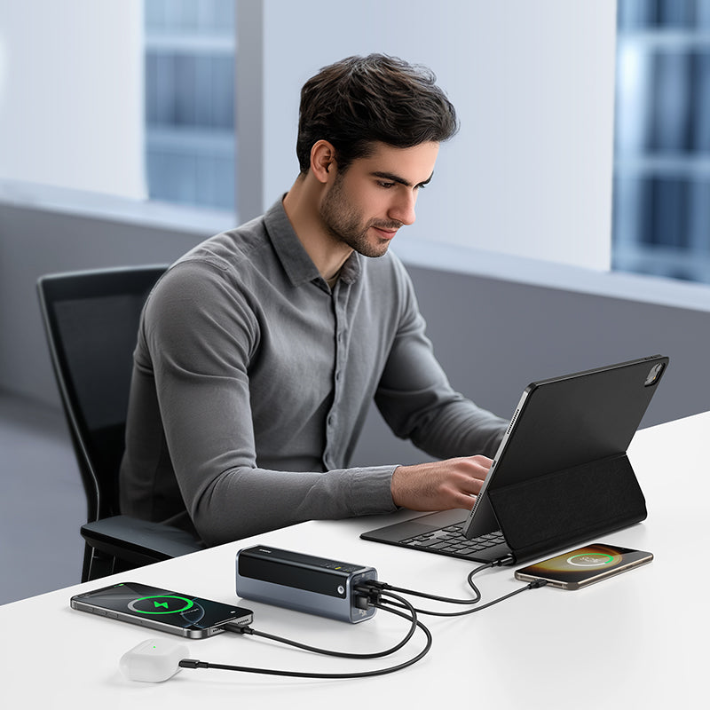 Man using a laptop with multiple devices connected to a power station in a modern office setting.