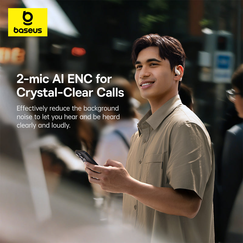 A man wearing a beige short-sleeve button-up shirt stands on a city street, smiling and holding a smartphone. He has a white wireless earbud in his ear.