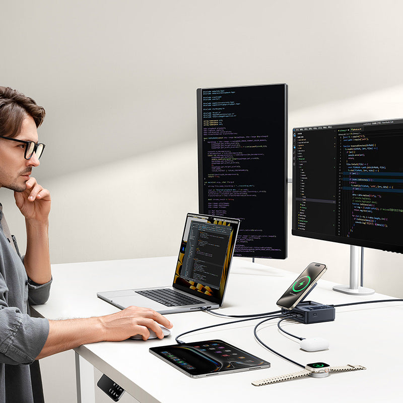 Person working at a desk with multiple electronic devices including a laptop, tablet, and smartphone.