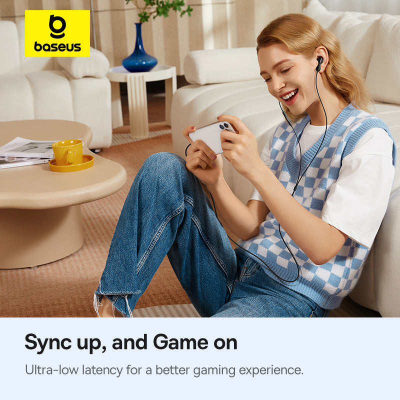 Woman sitting on a couch using a smartphone with earphones, Baseus logo visible