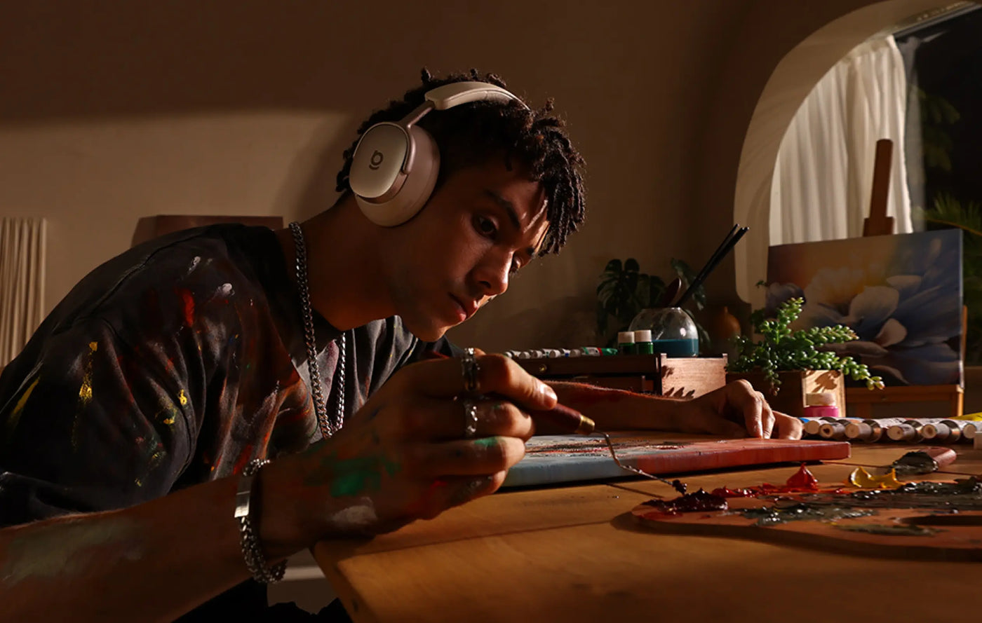 Person wearing headphones working on a craft project at a table in a cozy room.